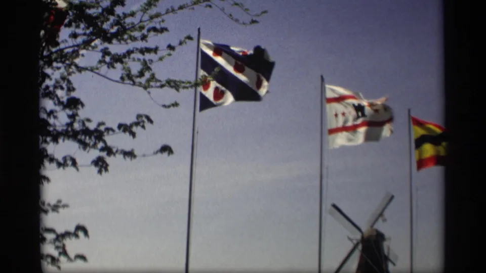 1969 Holland, Michigan 8mm frame showing multiple flags and a Dutch-style windmill beneath a clear sky.