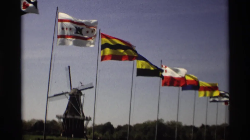 1969 Holland, Michigan frame with a Dutch-style windmill partly framed by a receding row of flags on tall poles.