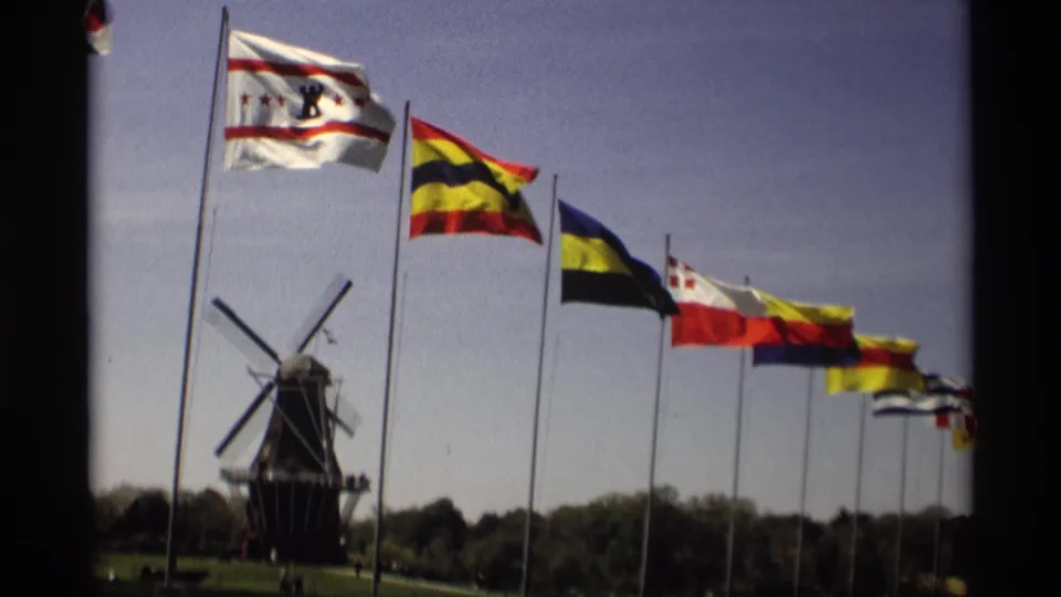 1969 Holland, Michigan home-movie frame emphasizing a white civic-style flag, striped flags, and a Dutch-style windmill beyond.