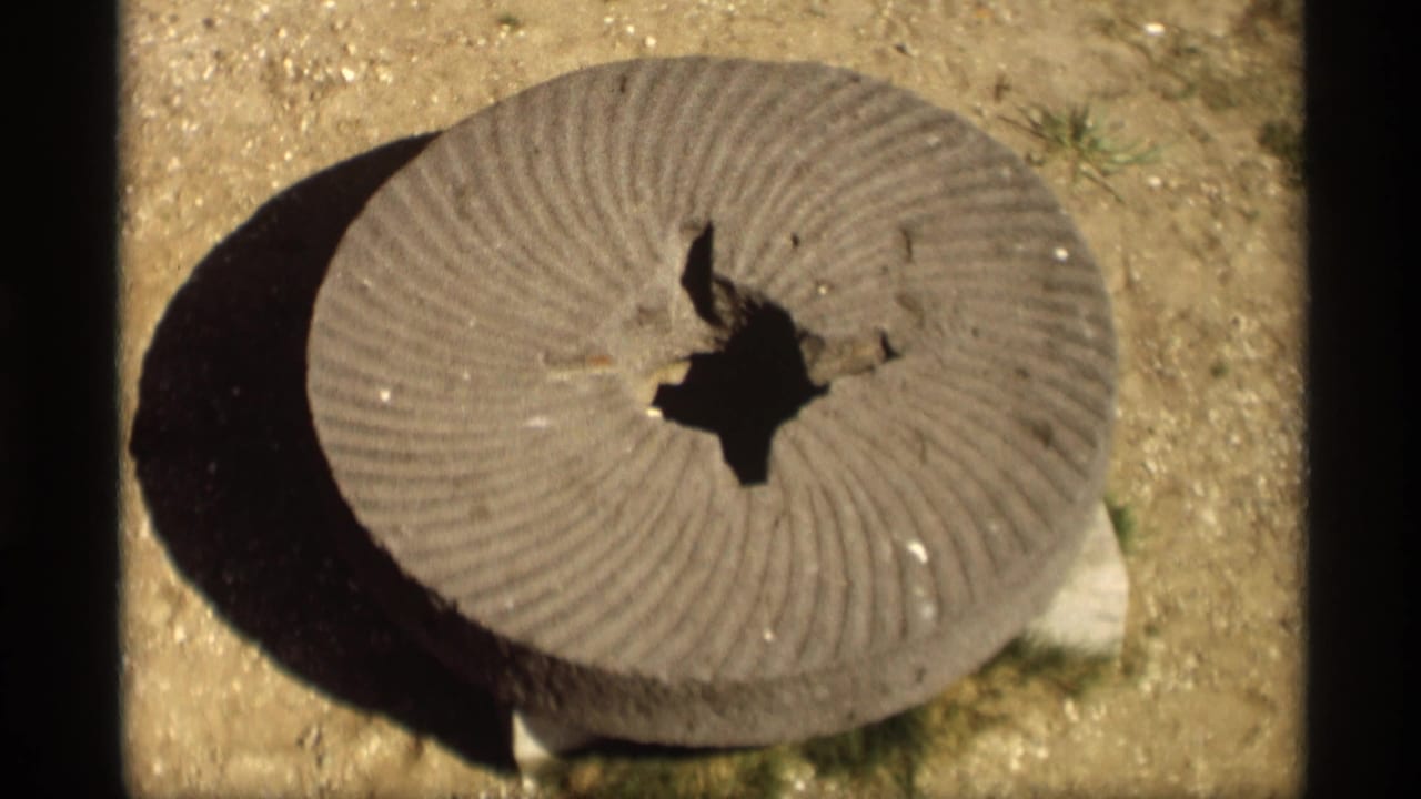 Grooved cement disk with a central hole resting on sandy ground in bright sunlight.