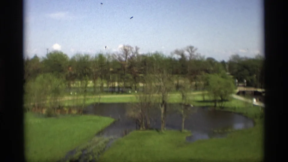 Elevated 1969 Holland, Michigan park view with a winding river or pond, bright lawns, leafing trees, paths, and distant structures.