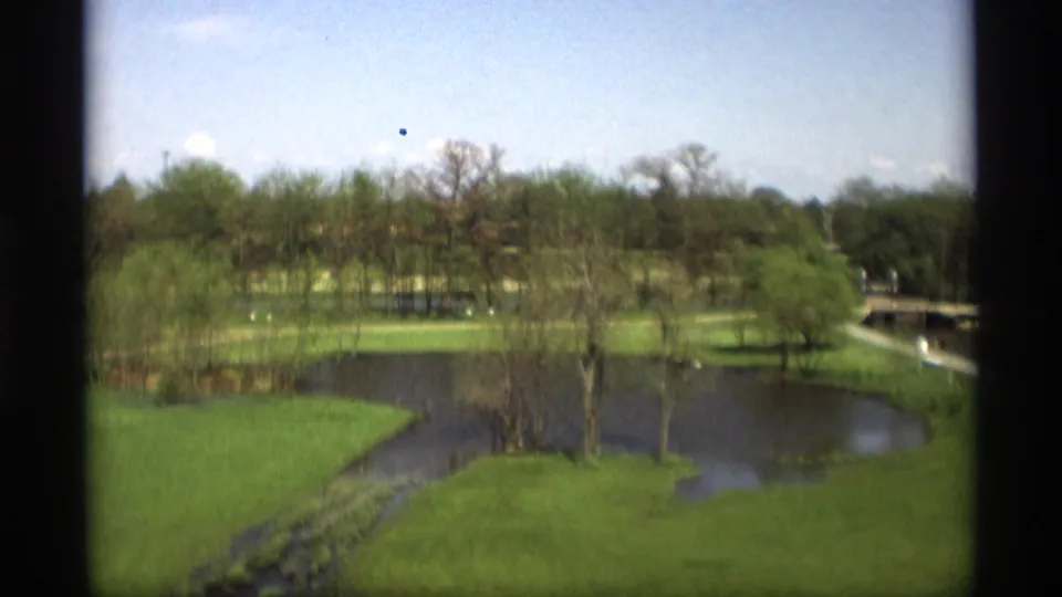 1969 8mm park view in Holland, Michigan, showing water curving through lawns, trees, paths, and small distant structures.