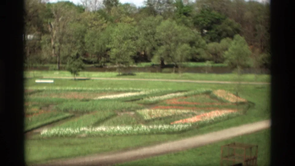 1969 Holland, Michigan 8mm view of geometric flower beds, grass, paths, and trees seen through dark vertical framing.