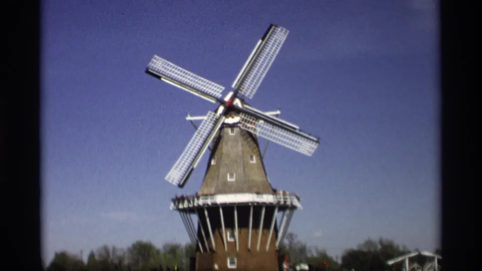 Final 8mm frame of the Holland, Michigan windmill, with crossed sails, brick base, and distant park visitors.