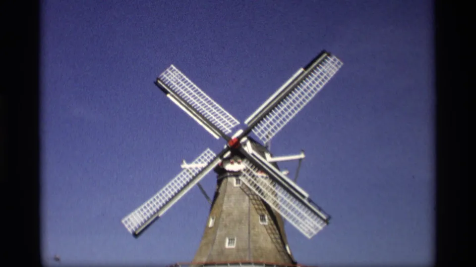 1969 Holland, Michigan 8mm frame showing a Dutch-style windmill from below, its white lattice blades angled across a clear blue sky.