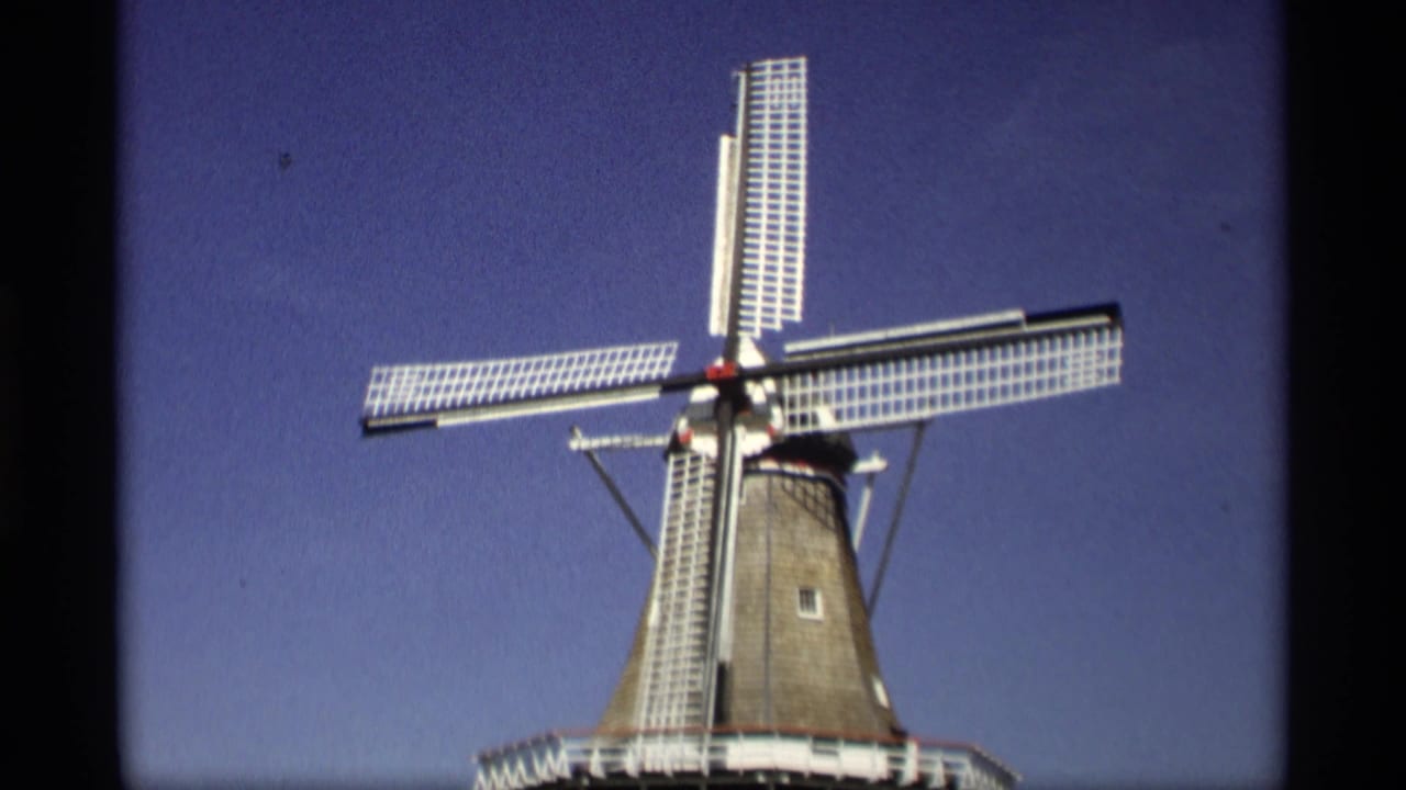 1969 8mm view in Holland, Michigan, showing a Dutch-style windmill with white lattice blades under a deep blue sky.