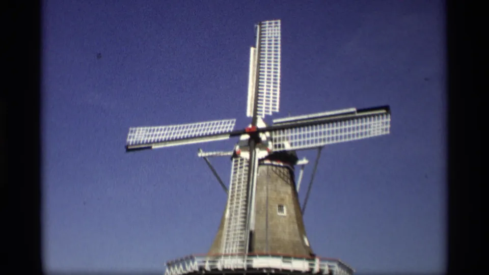1969 8mm view in Holland, Michigan, showing a Dutch-style windmill with white lattice blades under a deep blue sky.