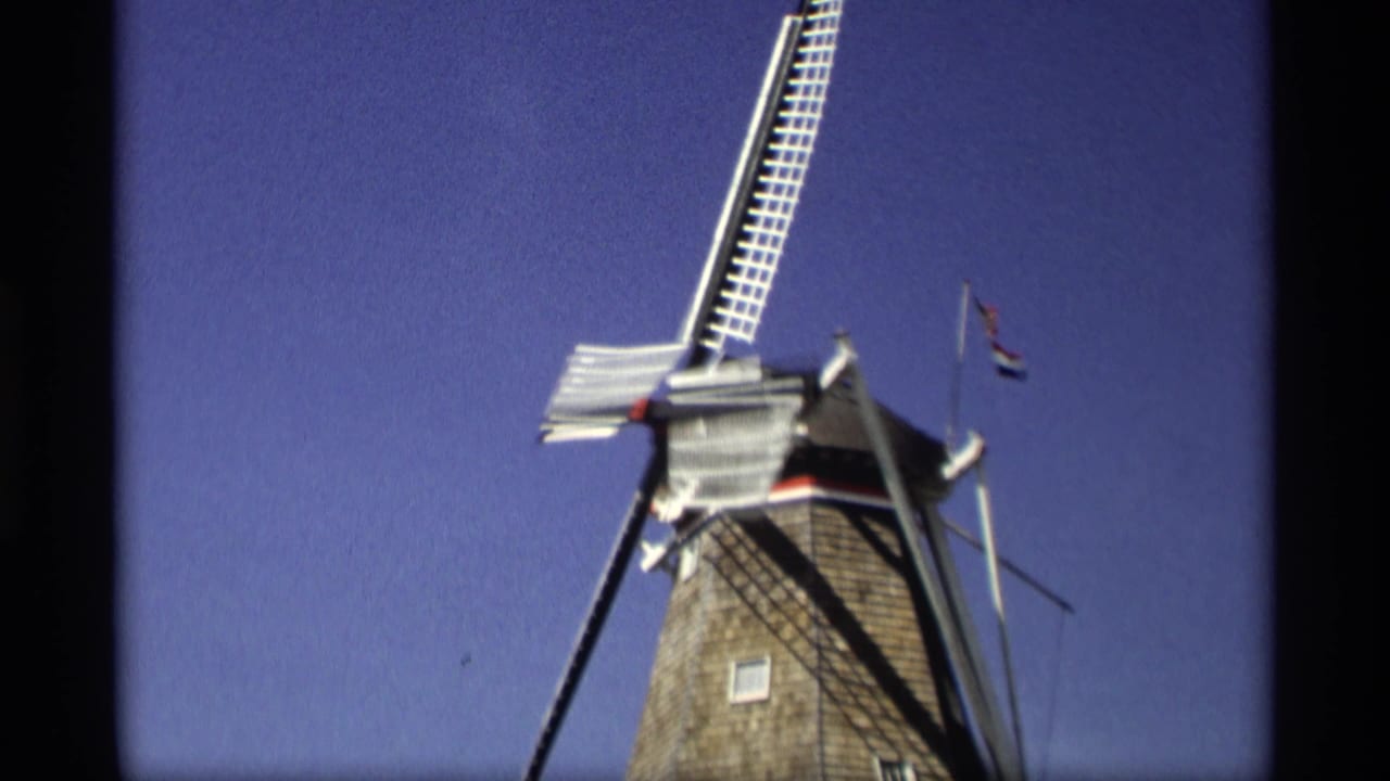 1969 8mm view in Holland, Michigan, looking up at a Dutch-style windmill with sails and a small flag against a blue sky.