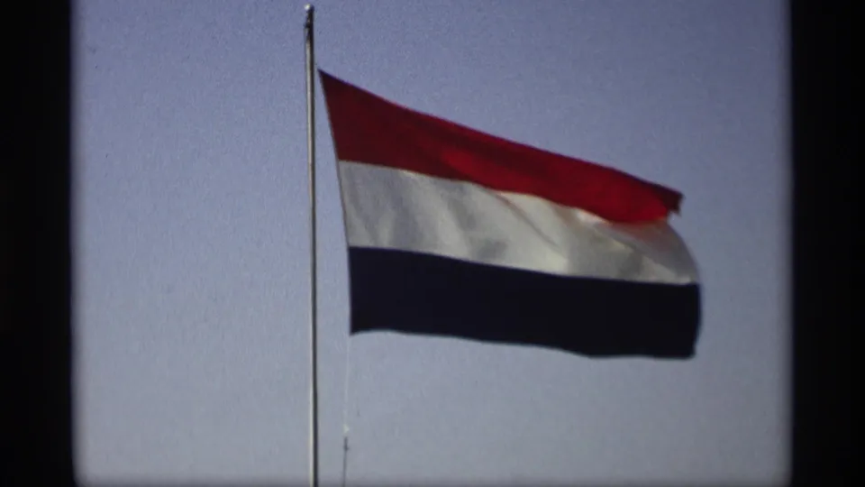 Wind lifts the Netherlands flag beside a tall pole in the supplied Holland, Michigan home-movie clip.