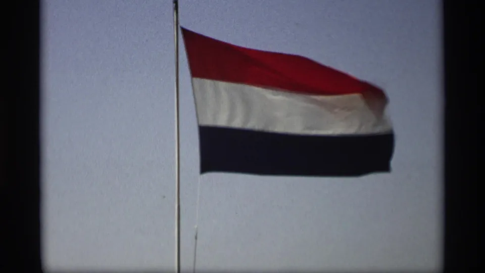 A close 8mm view shows the Netherlands flag rippling across the frame against a pale blue sky.