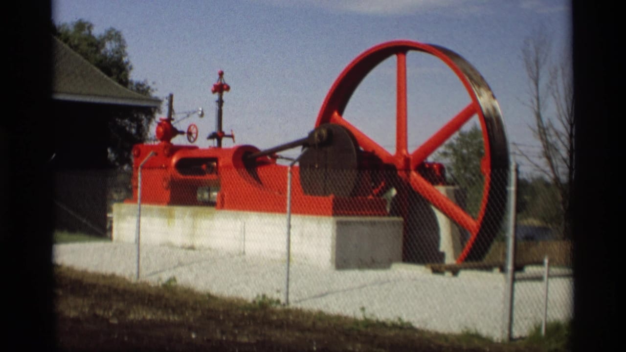 Red industrial machine with a large wheel behind a chain-link fence on a concrete slab.