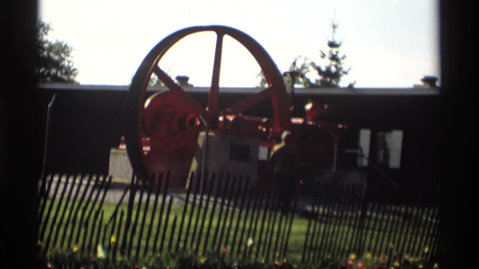 Backlit 8mm frame from Holland, Michigan showing the red industrial machine and wheel partly silhouetted near a fence.