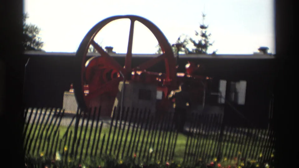 1969 Holland, Michigan 8mm frame showing a red industrial engine with a large flywheel behind a picket fence.