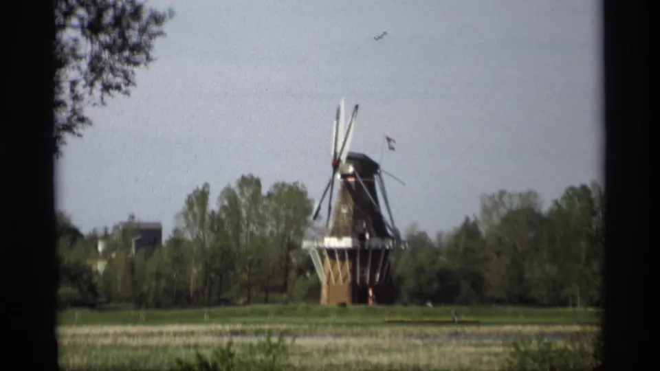 1969 Holland, Michigan 8mm frame of a Dutch-style windmill with an American flag, seen across a grassy field.