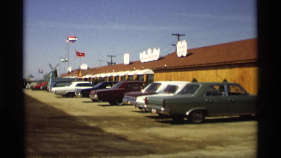 1969 Holland, Michigan frame showing classic American cars, flags, and a long roadside restaurant or market building.