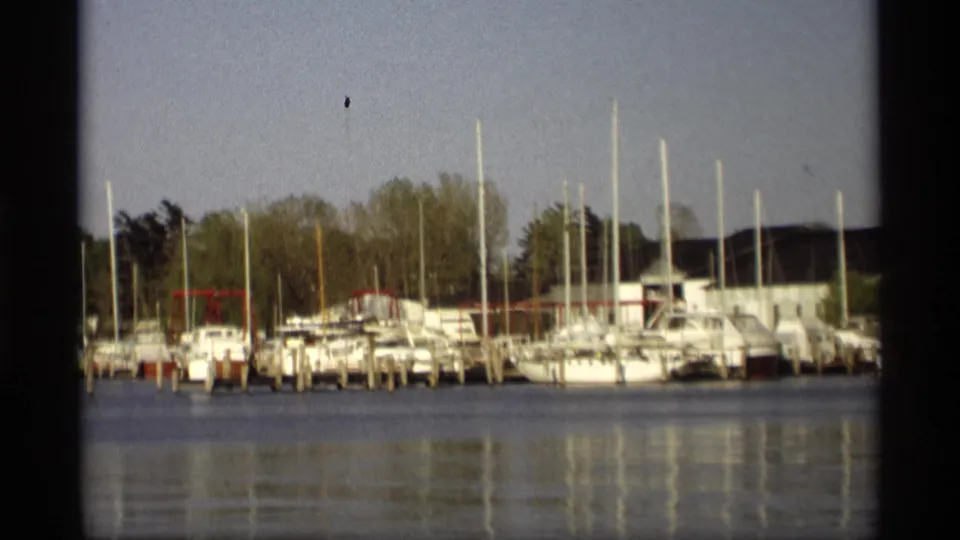 1969 Holland, Michigan 8mm frame with white sailboats and motorboats moored at docks, backed by trees and simple waterfront buildings.