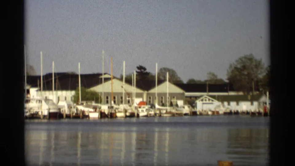 1969 Holland, Michigan 8mm frame showing pale marina buildings, docked boats, upright masts, and calm water reflections.