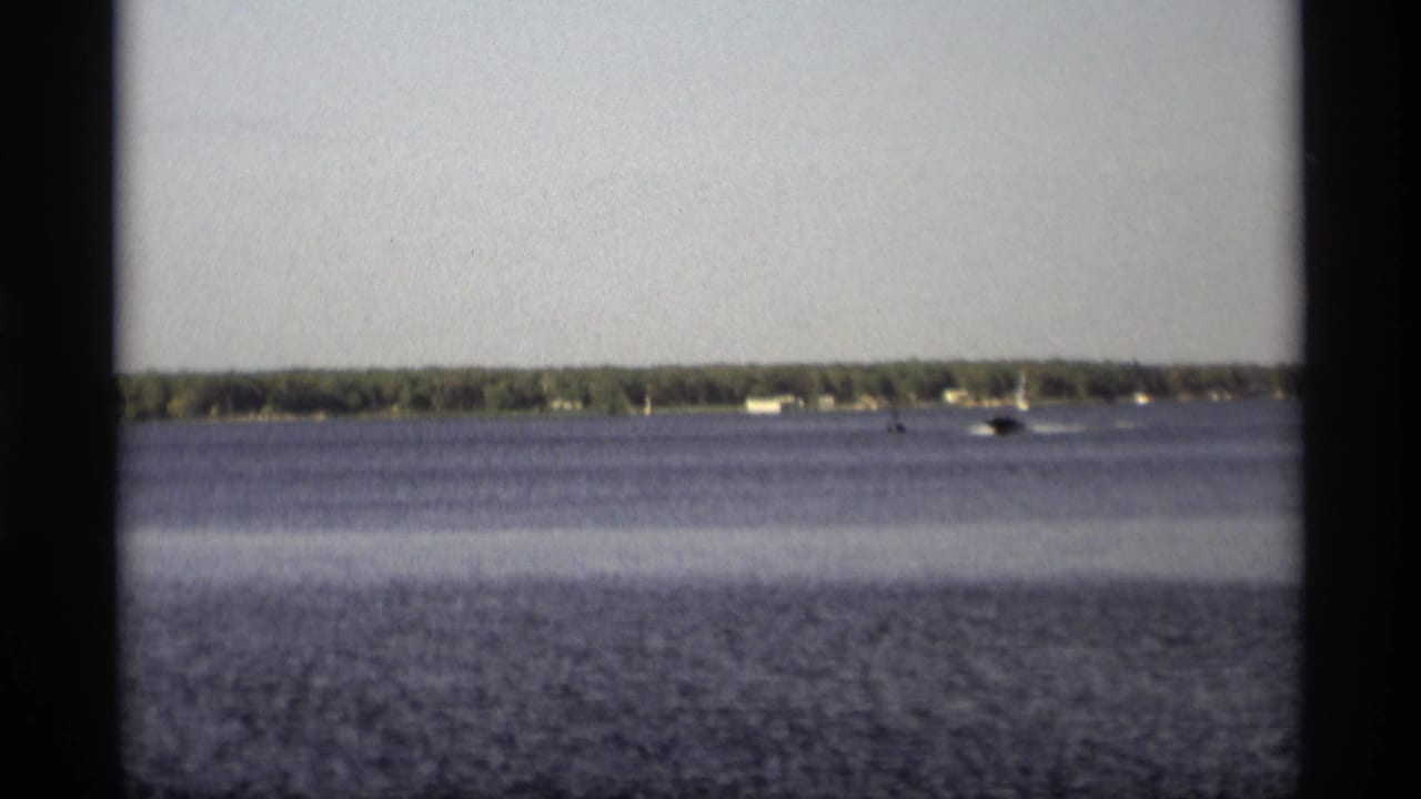 Motorboat crossing a lake near a distant wooded shoreline with houses.