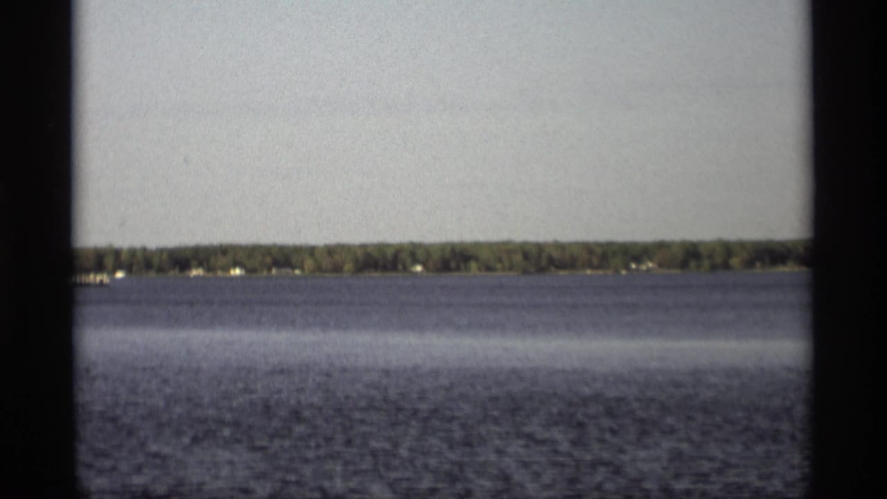 1969 Holland, Michigan 8mm frame showing open water and a distant tree-lined shoreline beneath a pale sky.