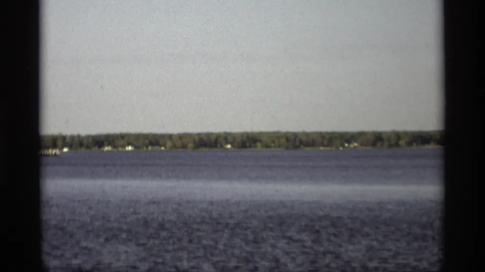 1969 Holland, Michigan 8mm frame showing open water and a distant tree-lined shoreline beneath a pale sky.