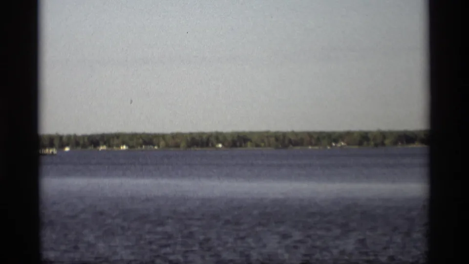 1969 Holland, Michigan home-movie frame with open water, distant trees, and a dark vertical film-frame edge.