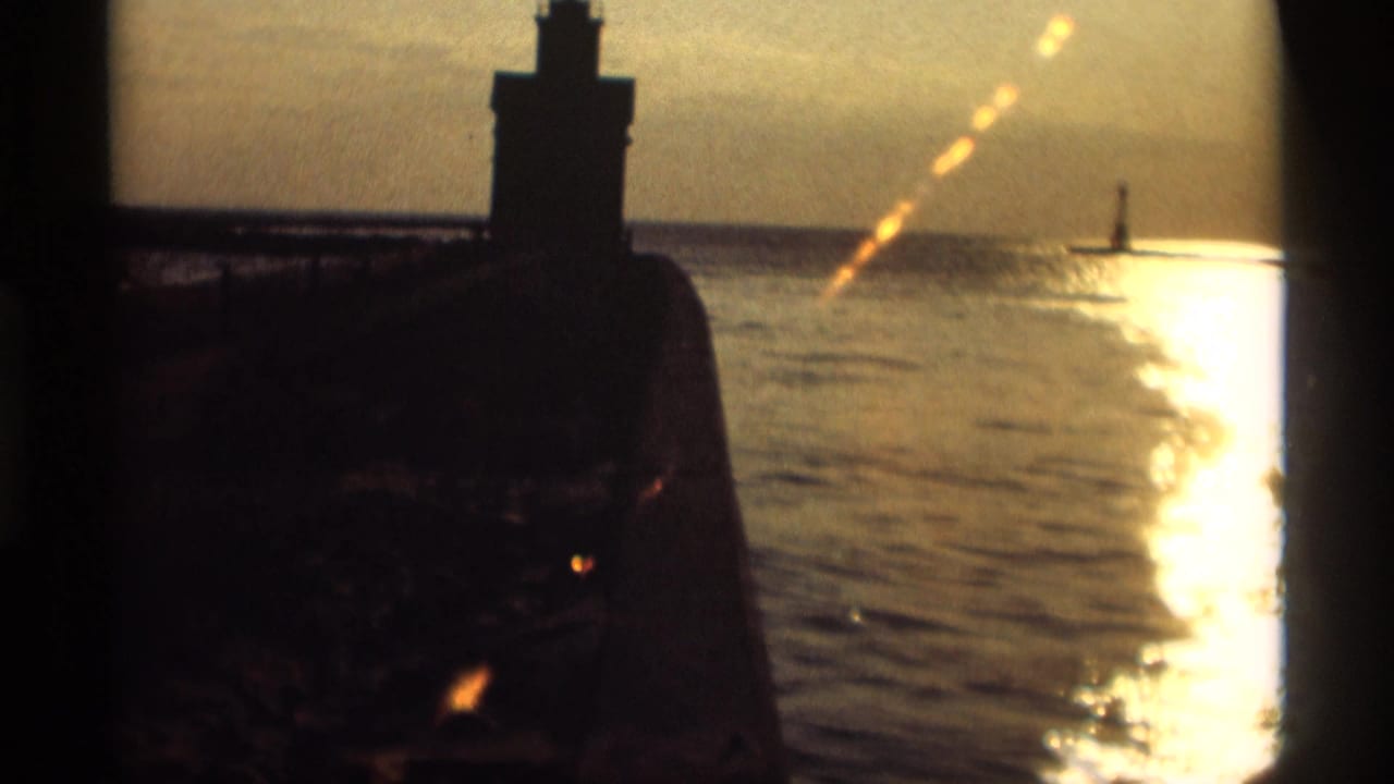 Silhouetted lighthouse on a pier beside sunlit lake water at sunset.