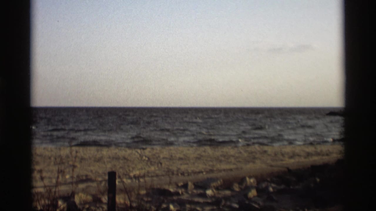 1969 8mm frame from Holland, Michigan showing choppy water, a sandy shore, and dark film edges.