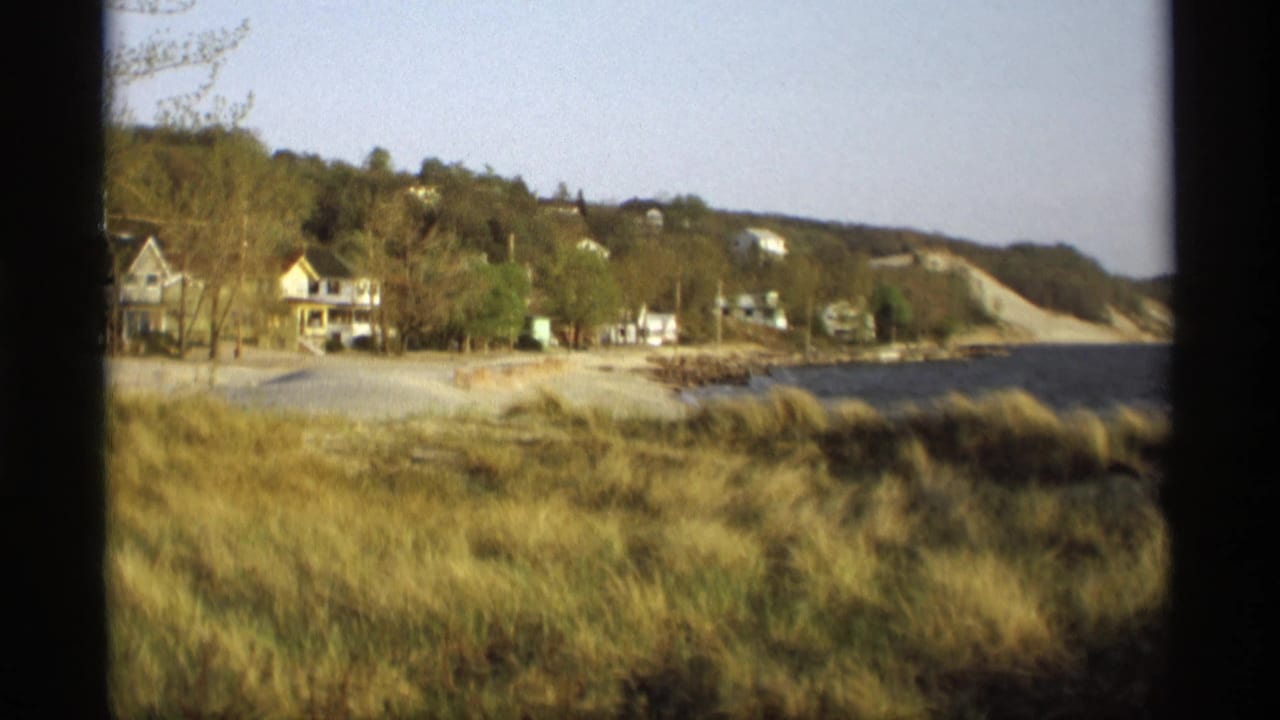 1969 Holland, Michigan lakeshore view with beach grass, white houses, trees, water, and a wooded slope.