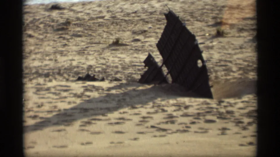The Holland, Michigan beach scene continues with a dark wooden structure casting across textured sand in warm 8mm light.