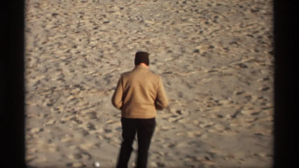 An adult man, seen from behind, walks across the sandy Holland, Michigan beach in 1969 home-movie footage.