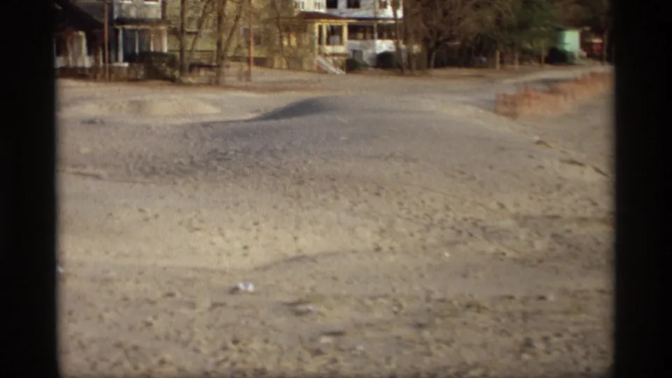 A sandy residential road in Holland, Michigan appears with modest houses and bare trees in the late-1960s home-movie frame.