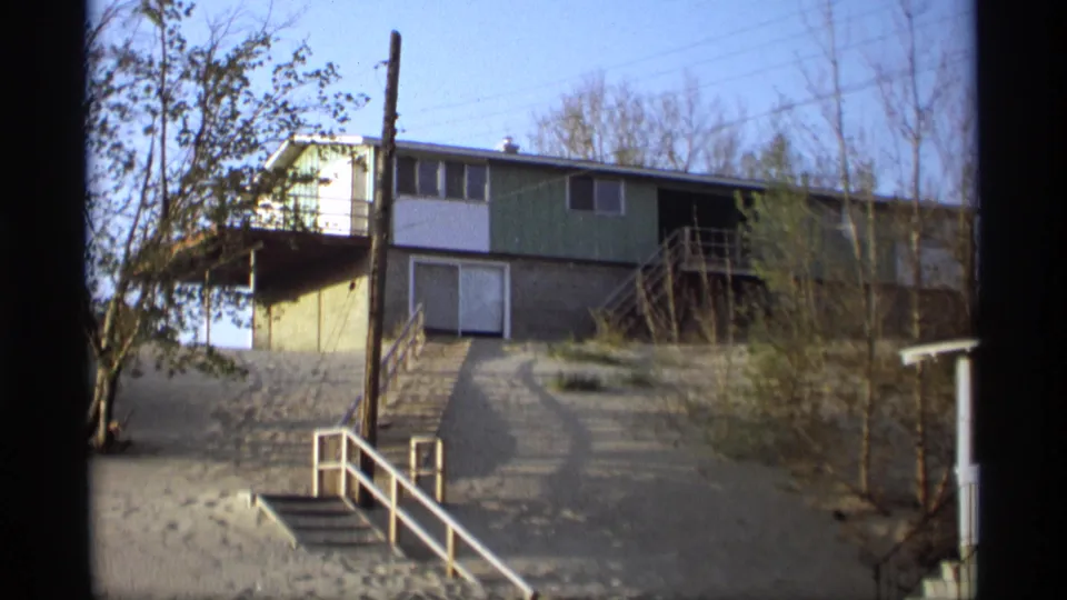 A green-and-white two-story house stands among sandy ground, stairs, railings, and bare trees in 1969 Holland, Michigan footage.