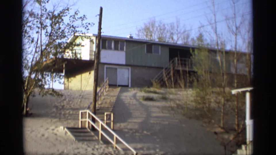 1969 Holland, Michigan 8mm view of a tan and green house on a sandy dune with white railings, steps, sparse trees, and blue sky.