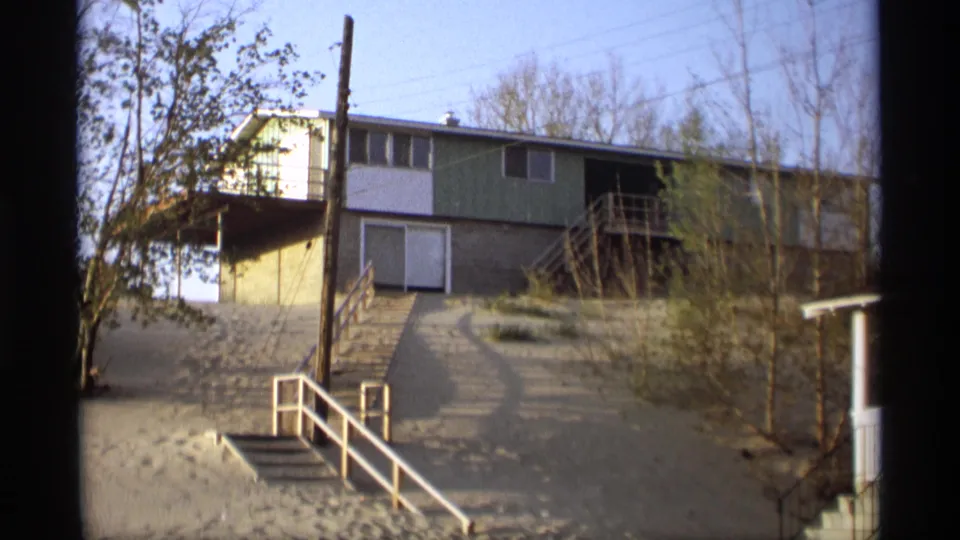 1969 Holland, Michigan exterior of a split-level house on sand, framed by a white stair rail, utility pole, bare trees, and clear daylight.