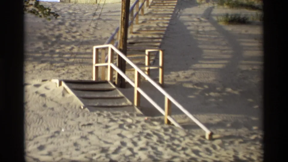 End frame of the 1969 Holland, Michigan exterior, focusing on white railings, wooden steps, sandy dune ground, walkway, and partial house above.