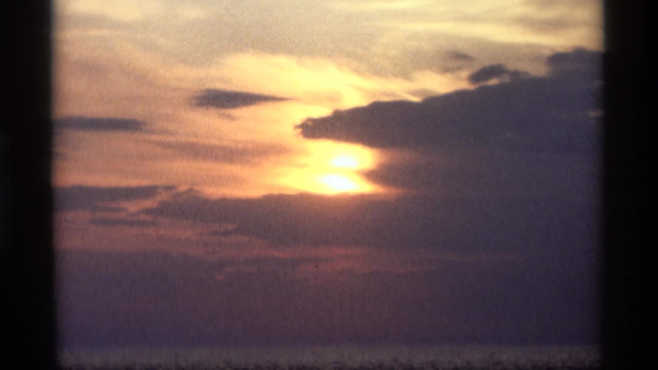 Low sun glowing through dark clouds in a blue-purple sky.