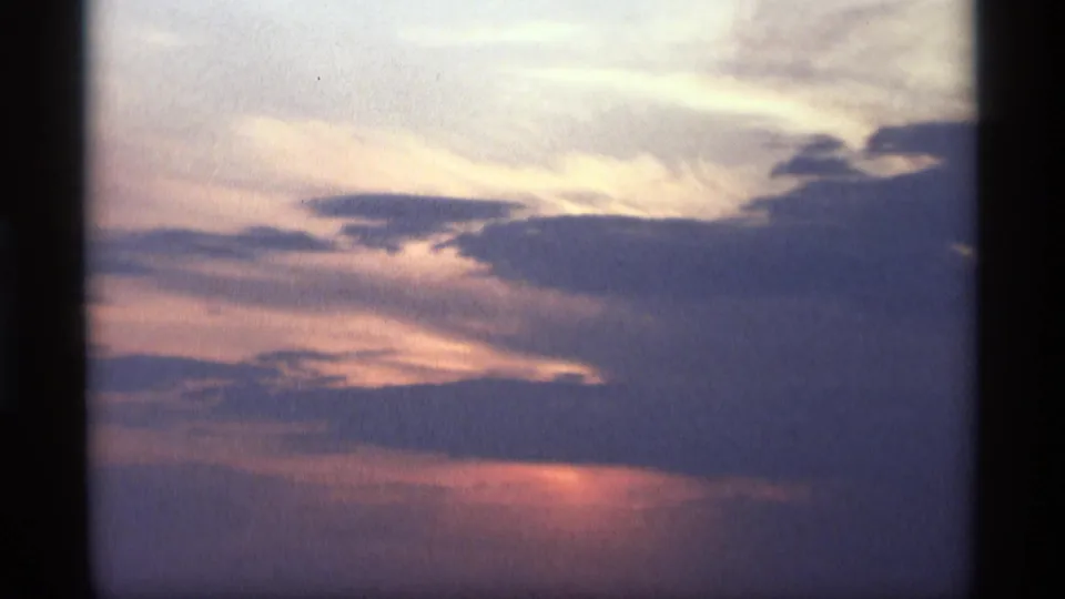 1969 8mm frame from Holland, Michigan showing a dimmer sunset sky with broad clouds and pink-purple horizon color.