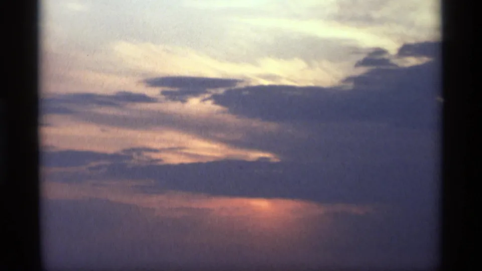 1969 Holland, Michigan 8mm frame showing the sunset fading behind dark cloud layers with a muted orange horizon.