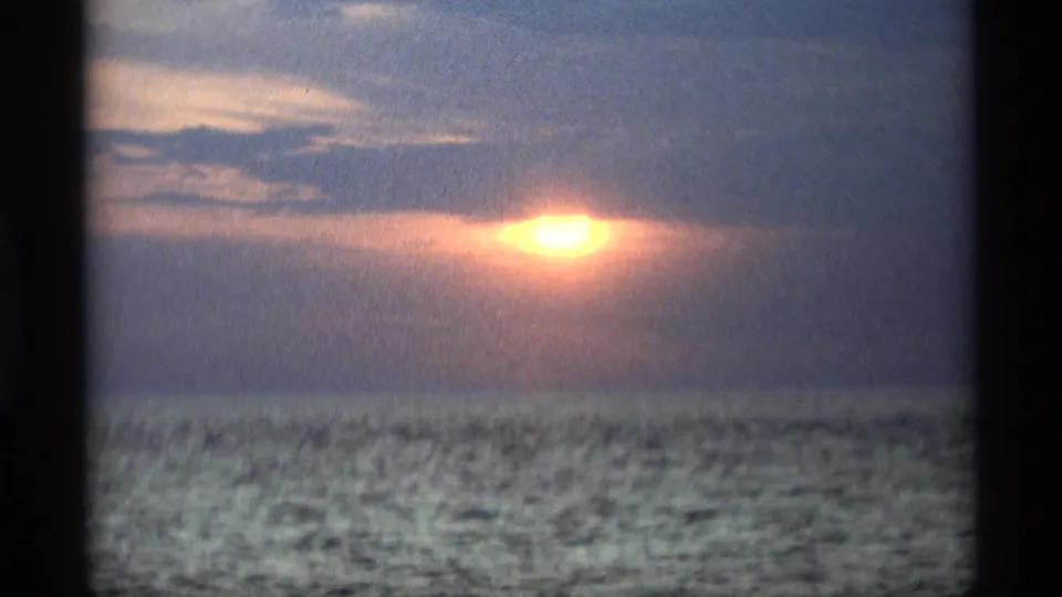 1969 Holland, Michigan home-movie frame with the sun brighter near the cloud edge over a calm-looking water horizon.