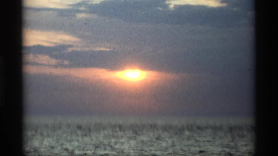 Final 1969 8mm frame from Holland, Michigan with the orange sun low behind clouds and open water below.