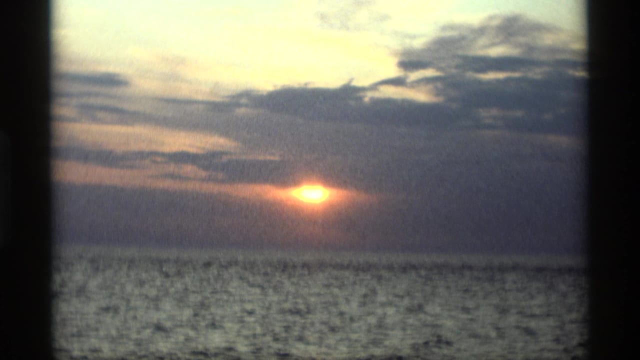 Sunset over open water with clouds and dark film borders.