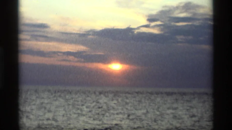 Vintage 8mm Holland, Michigan sunset view with the sun just above the waterline and heavy clouds across the sky.