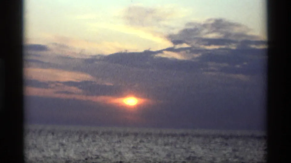 Final 8mm frame of the Holland, Michigan shoreline sunset, with the sun glowing low under broad clouds and water below.