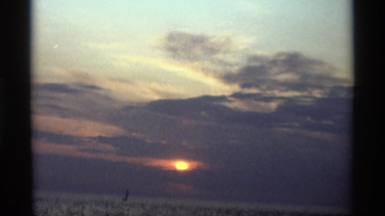 Sunset over open water with clouds and a small distant sail silhouette.