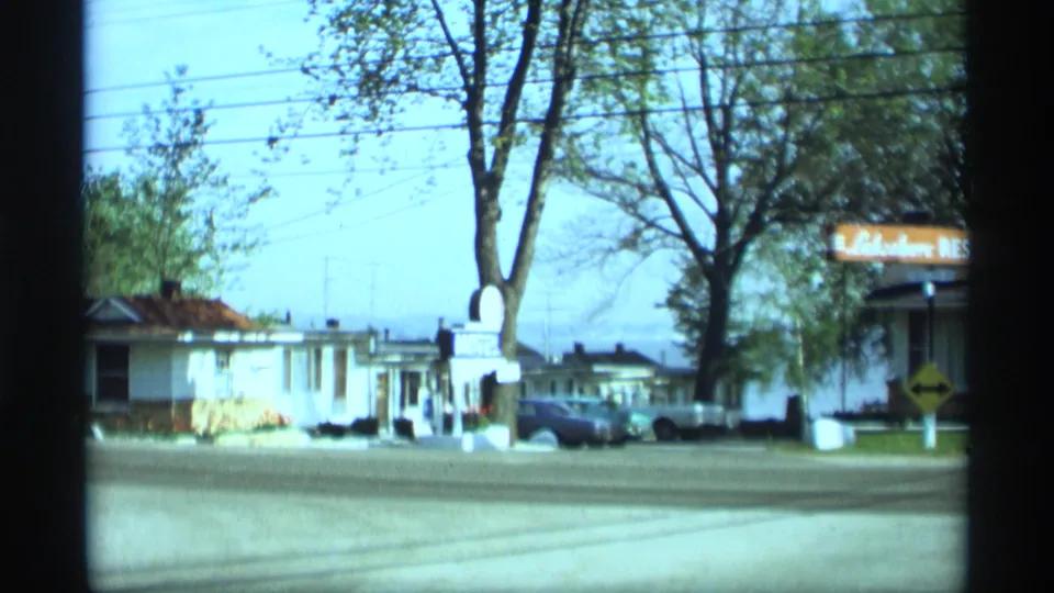 1969 Holland, Michigan roadside view with a motel sign, low buildings, parked cars, trees, and overhead utility lines.
