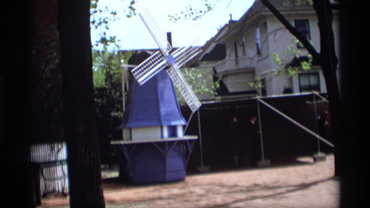 1969 Holland, Michigan 8mm frame showing a small blue-and-white Dutch-style windmill near trees, fencing, and a house.