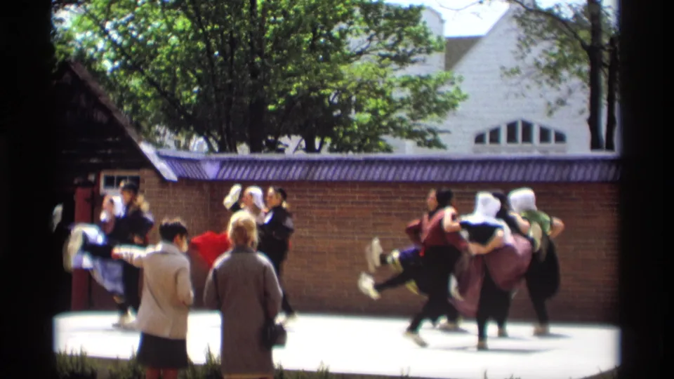 Costumed women in Holland, Michigan appear mid-dance in 1969, with spectators and trees visible around the outdoor stage.