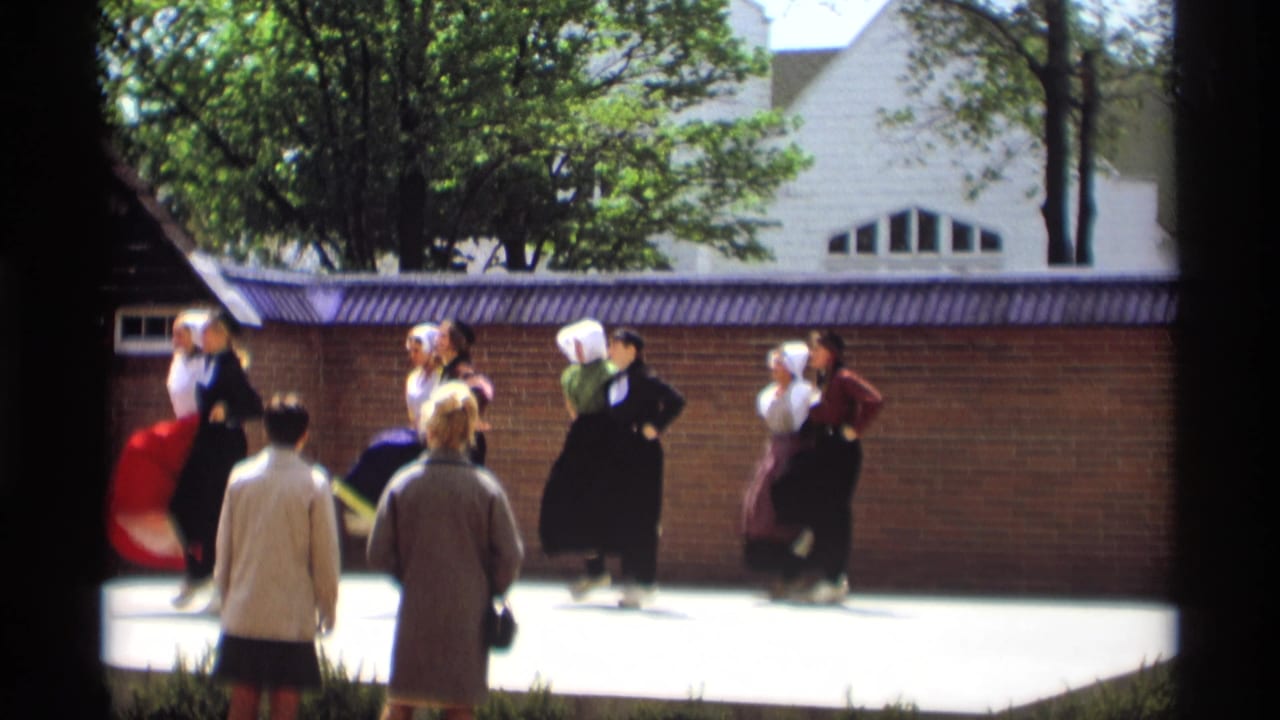 Dutch folk dancers perform in pairs while spectators watch from the foreground.