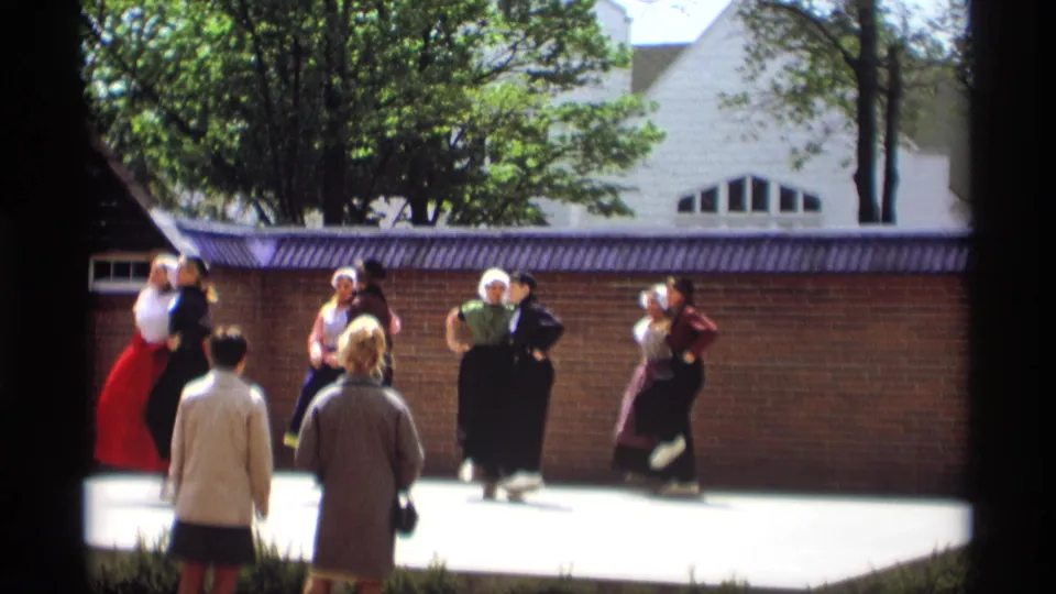 1969 Holland, Michigan frame showing Dutch-style folk dancers in paired motion on a sunlit outdoor stage.