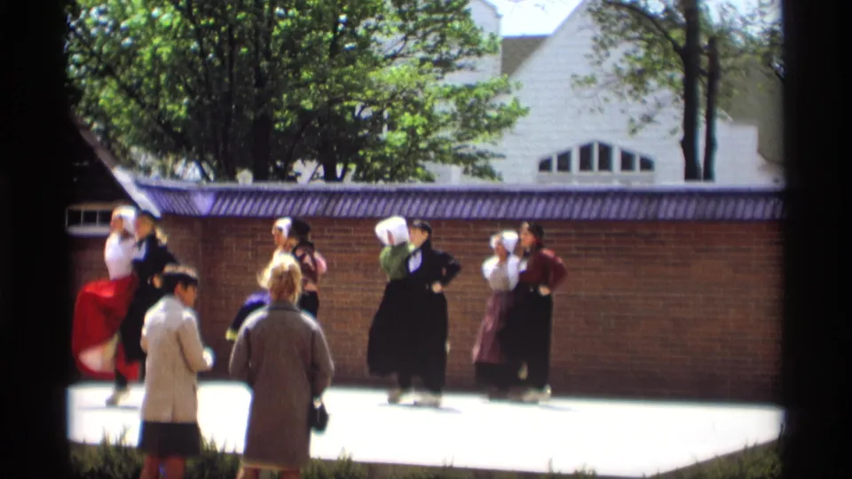 In Holland, Michigan in 1969, costumed women in white bonnets and long skirts perform a folk dance before spectators outdoors.